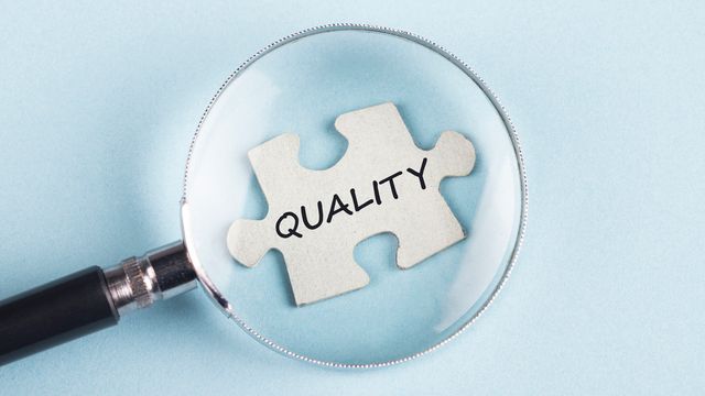 Magnifying glass placed over a jigsaw piece with the word "quality" written on it.